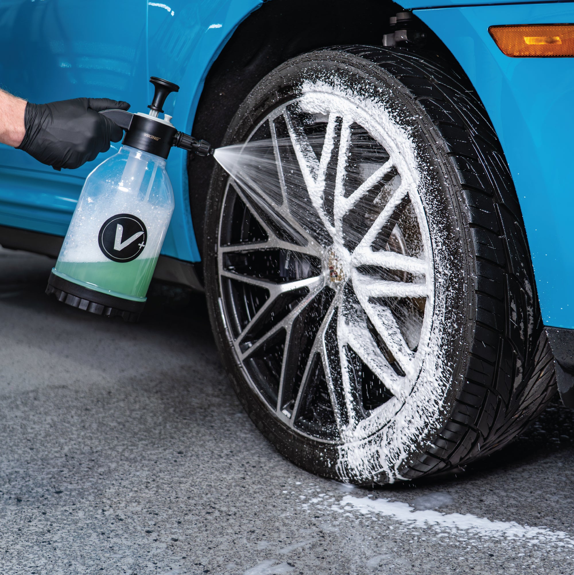 Person cleaning a car wheel with a Viking pump sprayer, focusing on the tire and rim.