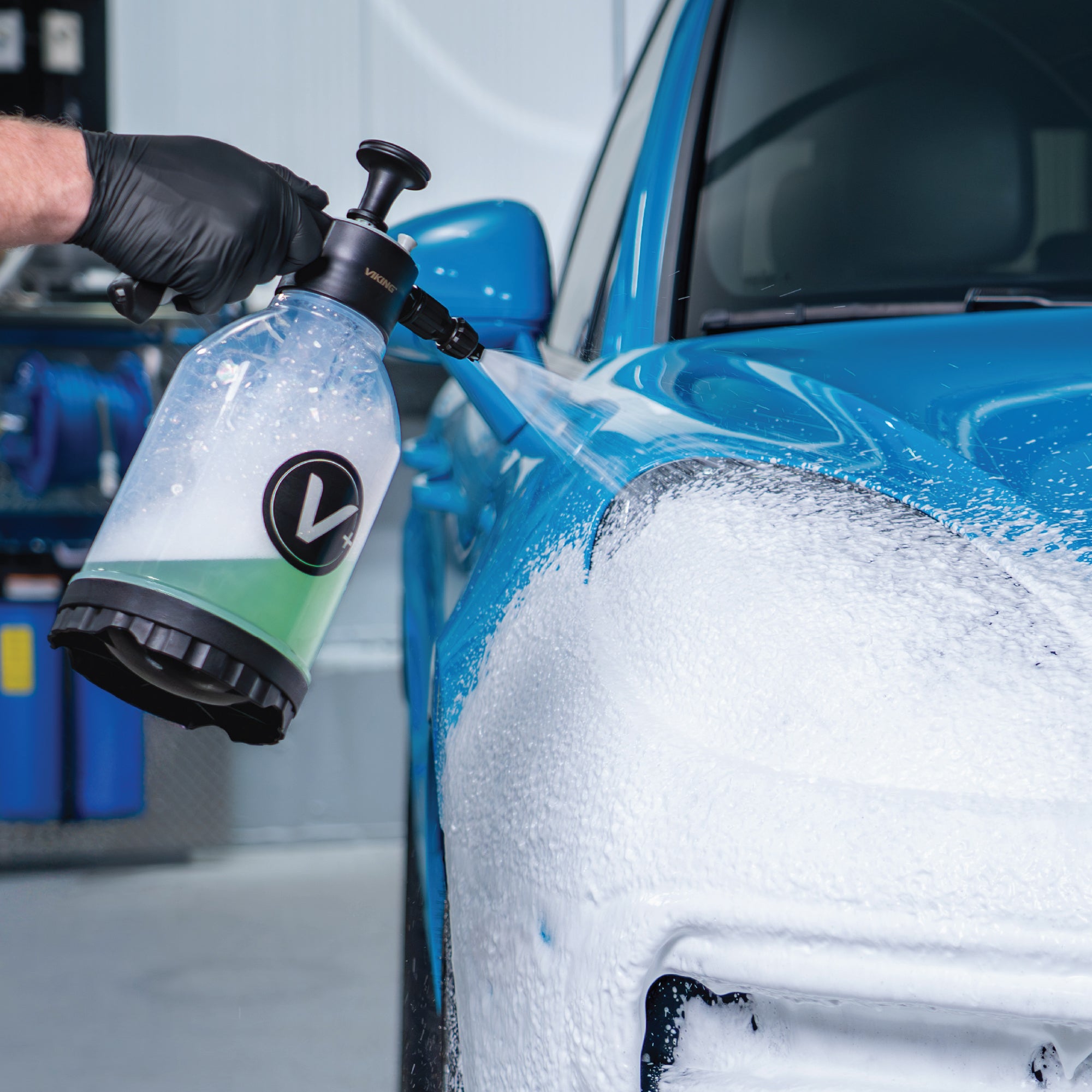 Person using a Viking pump sprayer to spray car wash soap onto a blue car